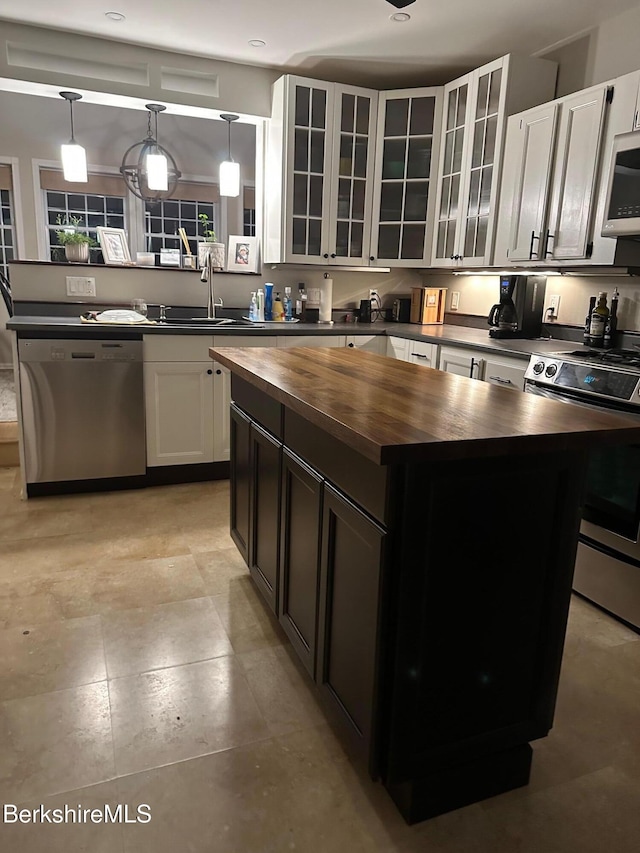 kitchen featuring appliances with stainless steel finishes, glass insert cabinets, a center island, hanging light fixtures, and wooden counters