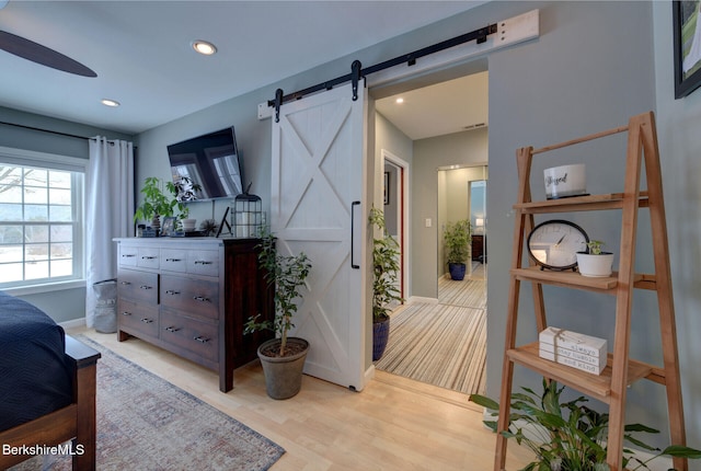 bedroom with light wood-style floors, recessed lighting, baseboards, and a barn door