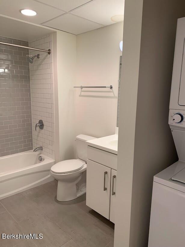 full bathroom featuring vanity, tile patterned floors, tiled shower / bath combo, toilet, and stacked washer / dryer