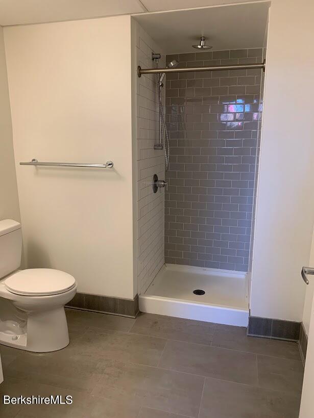 bathroom with tile patterned floors, toilet, and a tile shower
