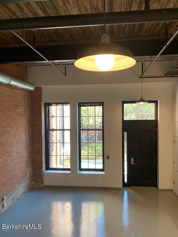 entrance foyer featuring wood ceiling, concrete flooring, beamed ceiling, and brick wall