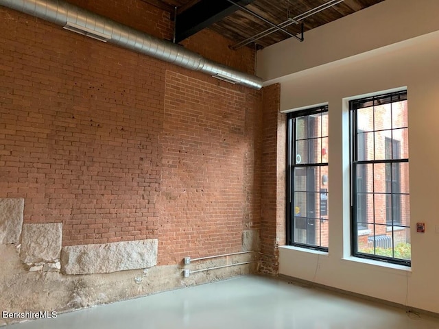 empty room with a wealth of natural light, a high ceiling, and brick wall
