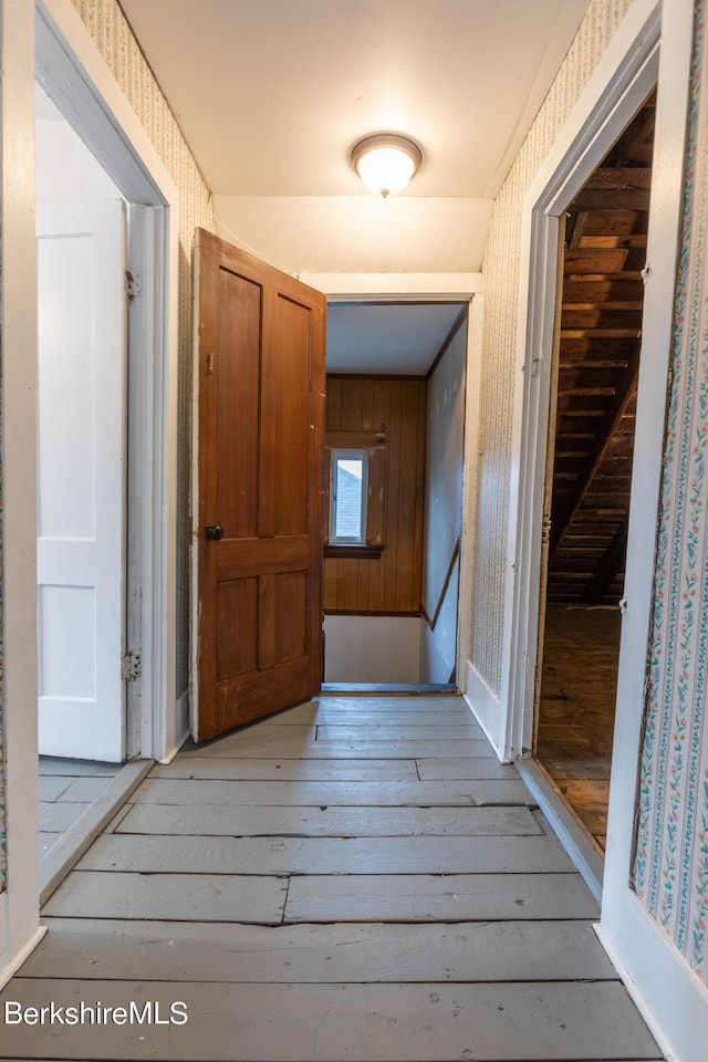 corridor with light wood-type flooring and wooden walls