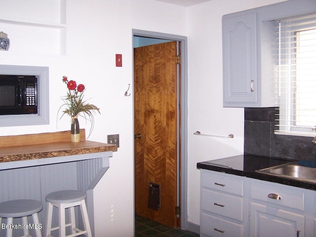 kitchen featuring black microwave, dark countertops, tasteful backsplash, a sink, and white cabinets