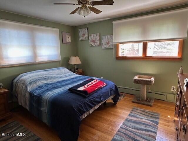 bedroom with a baseboard radiator, multiple windows, wood finished floors, and ceiling fan