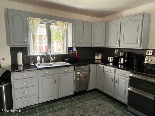 kitchen with dark tile patterned floors, a sink, dark countertops, and stainless steel appliances