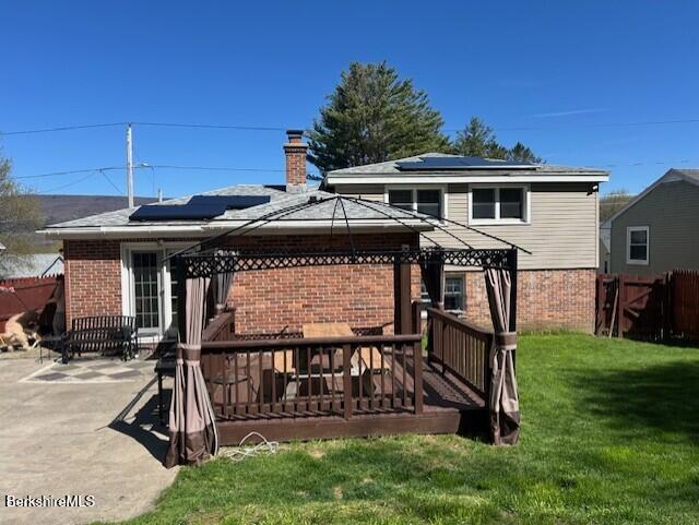 rear view of property featuring a yard, brick siding, a gazebo, and roof mounted solar panels