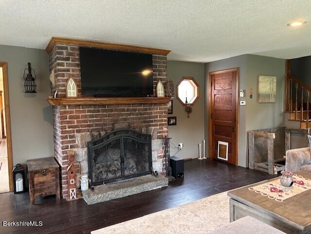 living room with dark hardwood / wood-style flooring, a textured ceiling, and a brick fireplace