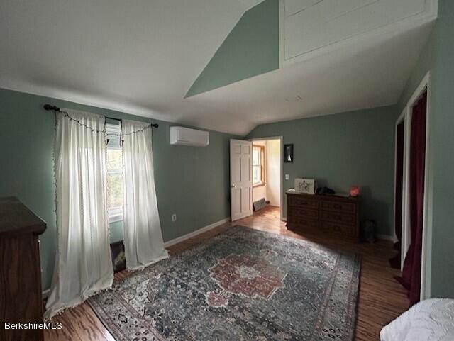 bedroom with light hardwood / wood-style flooring, an AC wall unit, and lofted ceiling