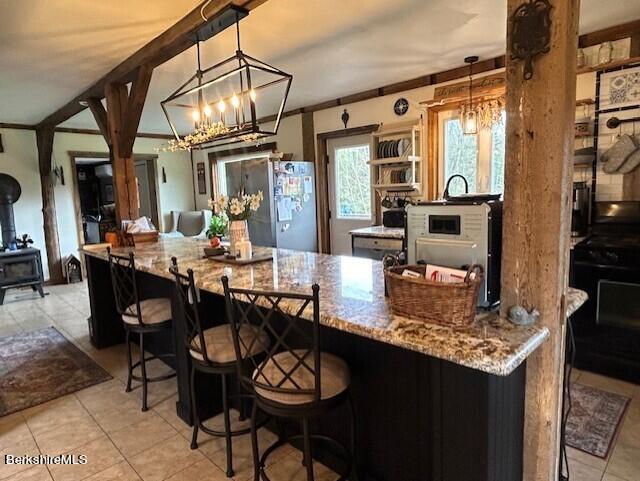 kitchen with stainless steel refrigerator, a chandelier, pendant lighting, a kitchen bar, and black range