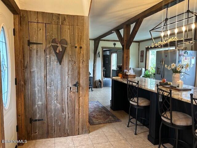 kitchen with light stone counters, decorative light fixtures, light tile patterned flooring, a kitchen bar, and stainless steel fridge with ice dispenser