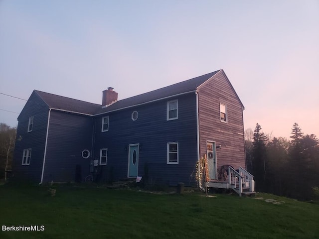 back house at dusk featuring a lawn