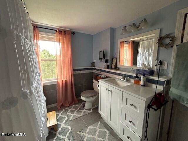 bathroom featuring tile patterned flooring, vanity, toilet, and tile walls