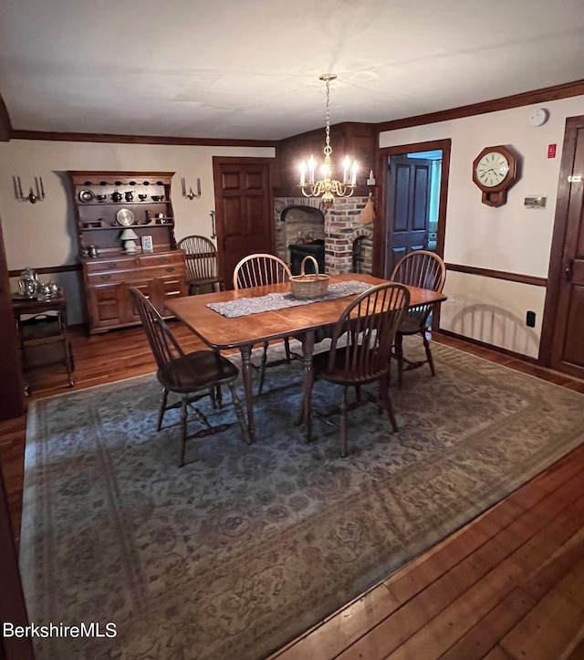 dining space with dark hardwood / wood-style floors, crown molding, a fireplace, and a chandelier