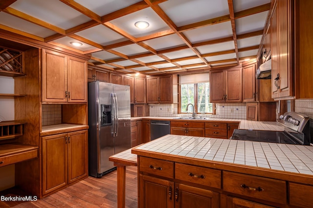 kitchen with coffered ceiling, sink, light hardwood / wood-style flooring, tile counters, and stainless steel appliances