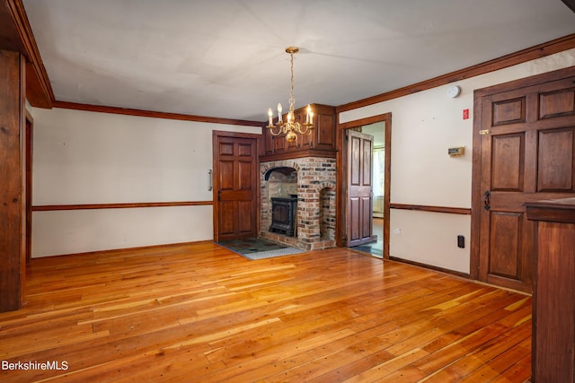 unfurnished living room featuring a notable chandelier, light hardwood / wood-style floors, a wood stove, and ornamental molding