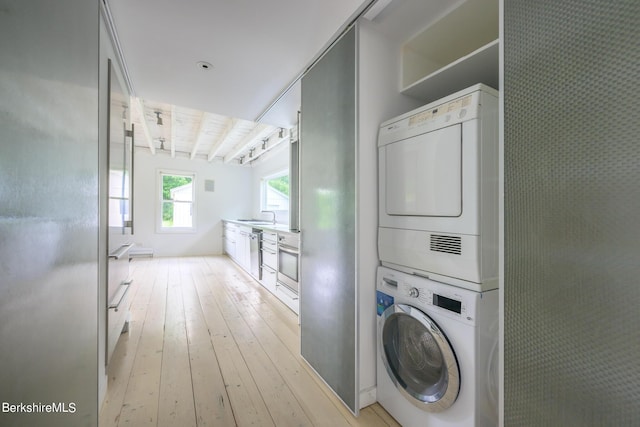 laundry area featuring light wood-type flooring, stacked washer and dryer, and sink