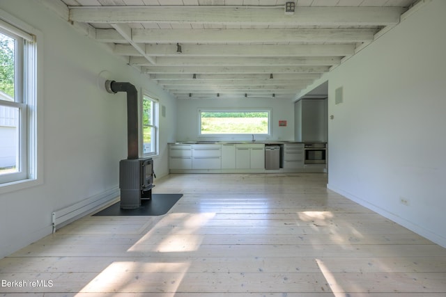 unfurnished room with light wood-type flooring, a wood stove, a baseboard heating unit, and sink