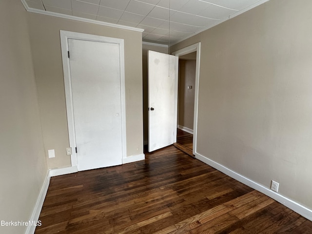 unfurnished bedroom featuring crown molding and dark wood-type flooring