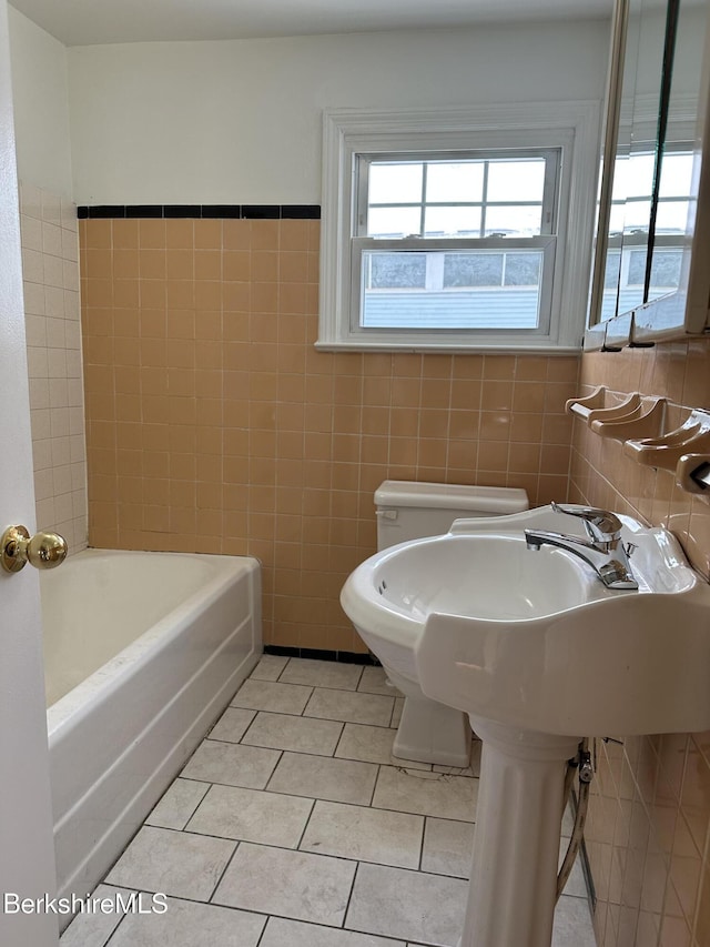 bathroom featuring tile patterned flooring, a tub to relax in, toilet, and tile walls