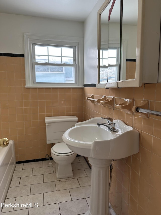 bathroom featuring tile patterned flooring, tile walls, a bathtub, and toilet