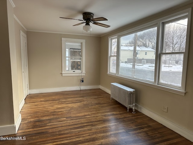 spare room with radiator, dark wood-type flooring, a wealth of natural light, and ornamental molding