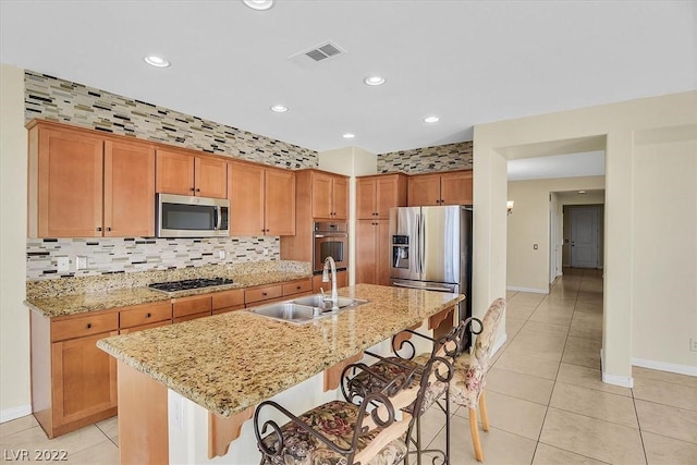 kitchen featuring an island with sink, sink, appliances with stainless steel finishes, a breakfast bar, and tasteful backsplash