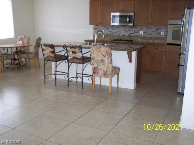 kitchen with sink, light tile floors, a breakfast bar, backsplash, and stainless steel appliances