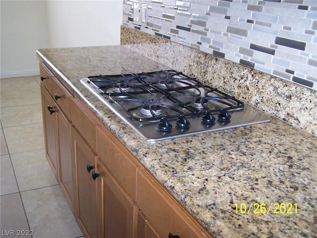 kitchen with stainless steel gas stovetop, light tile flooring, tasteful backsplash, and light stone countertops