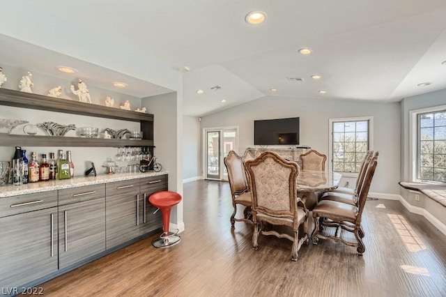 dining space with bar, wood-type flooring, and vaulted ceiling