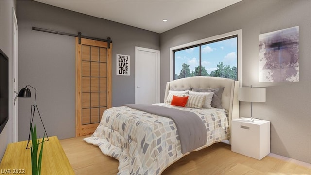 bedroom with a barn door and light hardwood / wood-style flooring