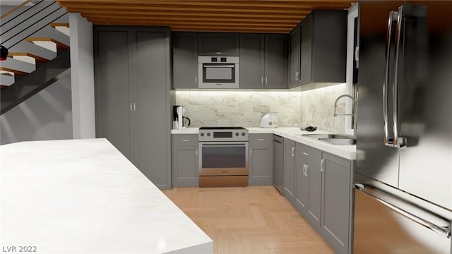 kitchen with light parquet floors, stainless steel appliances, backsplash, gray cabinetry, and sink