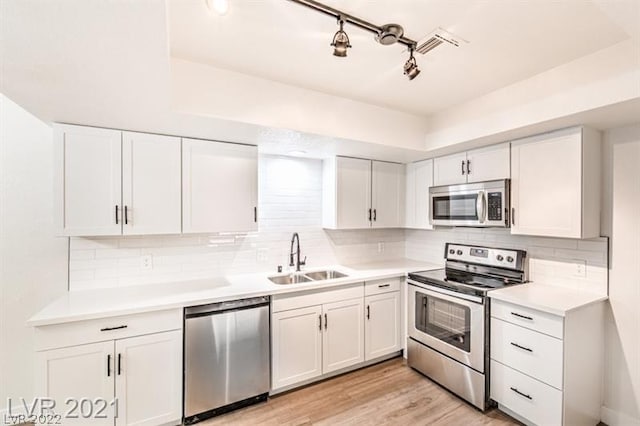 kitchen with appliances with stainless steel finishes, white cabinets, backsplash, light wood-type flooring, and sink