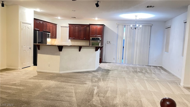 kitchen featuring decorative light fixtures, an inviting chandelier, a kitchen bar, light carpet, and stainless steel oven