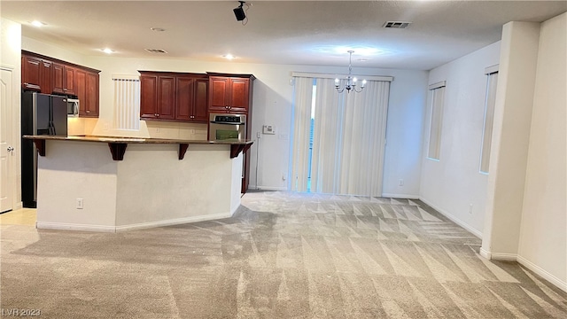 kitchen with an inviting chandelier, a kitchen bar, appliances with stainless steel finishes, and light carpet