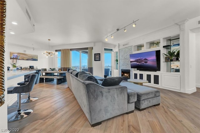 living room featuring a chandelier, light hardwood / wood-style flooring, decorative columns, track lighting, and a large fireplace