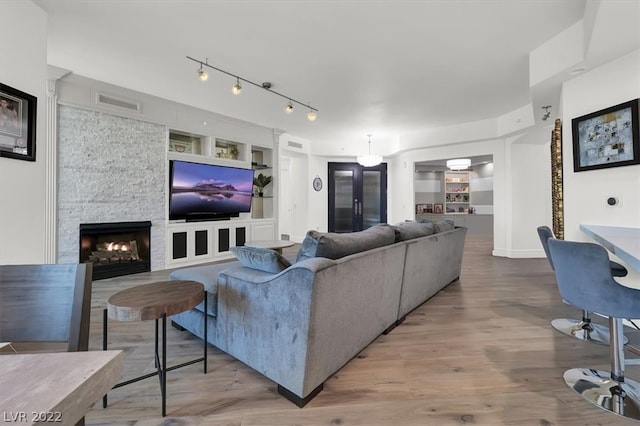 living room with built in features, light hardwood / wood-style floors, a stone fireplace, a chandelier, and rail lighting