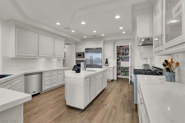 kitchen featuring an island with sink, white cabinetry, light wood-type flooring, and built in appliances