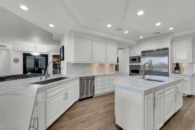 kitchen featuring built in appliances, sink, white cabinets, backsplash, and light wood-type flooring