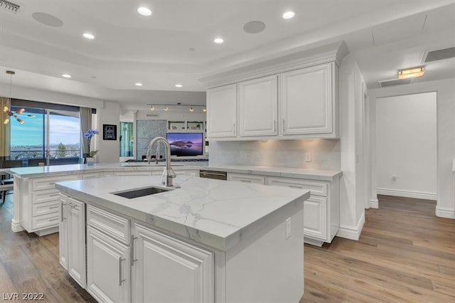 kitchen with decorative light fixtures, white cabinetry, light hardwood / wood-style flooring, and a kitchen island with sink