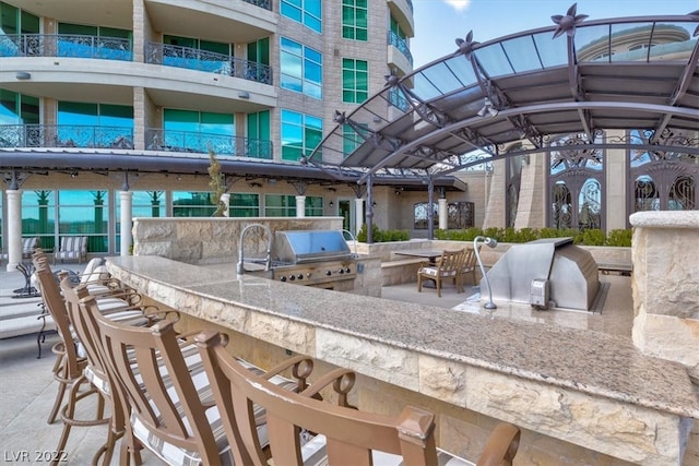 view of patio featuring a balcony, exterior kitchen, an outdoor bar, and a grill