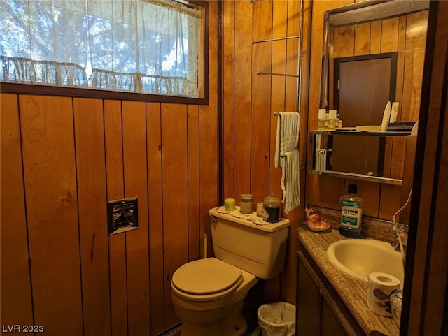 bathroom with wood walls, toilet, and vanity with extensive cabinet space