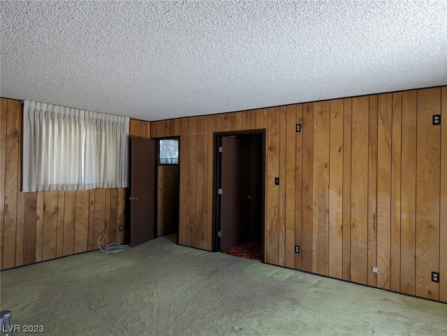 carpeted spare room with wood walls and a textured ceiling