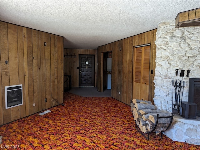 interior space featuring wooden walls, a textured ceiling, dark carpet, and a fireplace