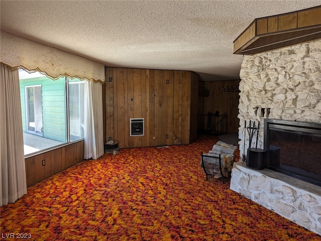 living room featuring a stone fireplace, wood walls, a textured ceiling, and dark colored carpet