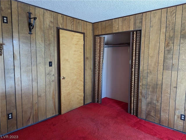 unfurnished bedroom featuring a closet, dark colored carpet, and wood walls