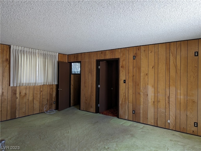 spare room with a textured ceiling, wood walls, and dark carpet