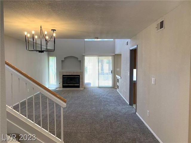 unfurnished living room featuring an inviting chandelier, a textured ceiling, carpet, and a fireplace