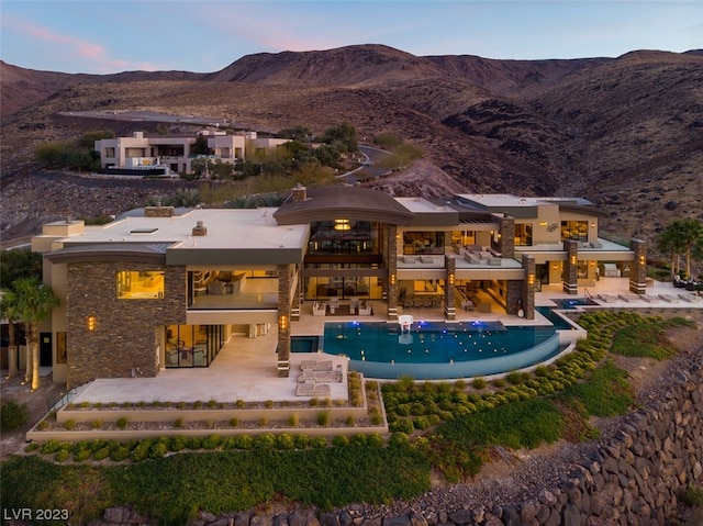 back house at dusk with a mountain view and a patio