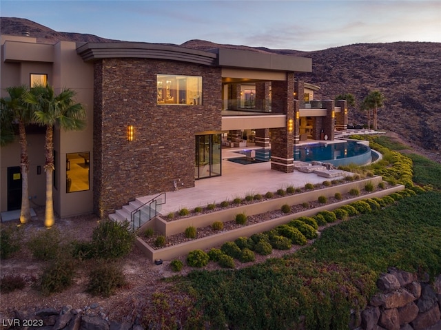 back house at dusk with a mountain view and a patio area